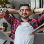 Joyful businessman in casual sitting in his office and resting from work from multitasking